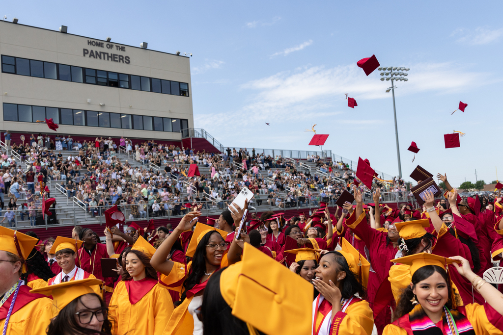 Putnam City North graduates toss their caps into the air as the crowd cheers from the stadium bleachers.