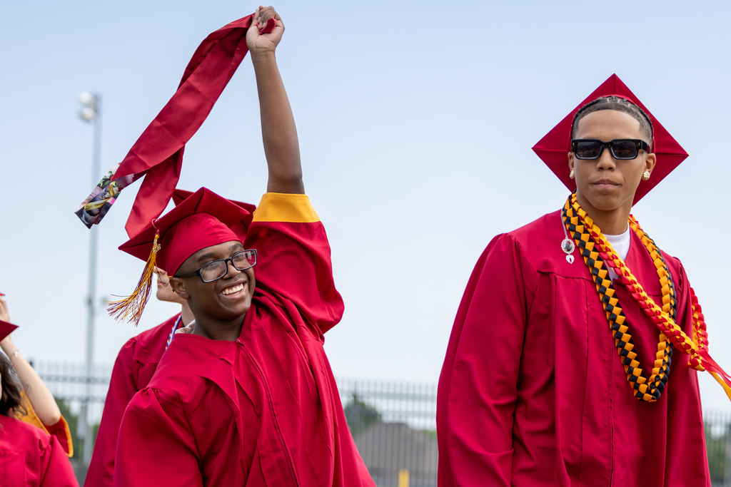 Two Putnam City North graduates celebrate, with one raising a cap in the air and smiling.