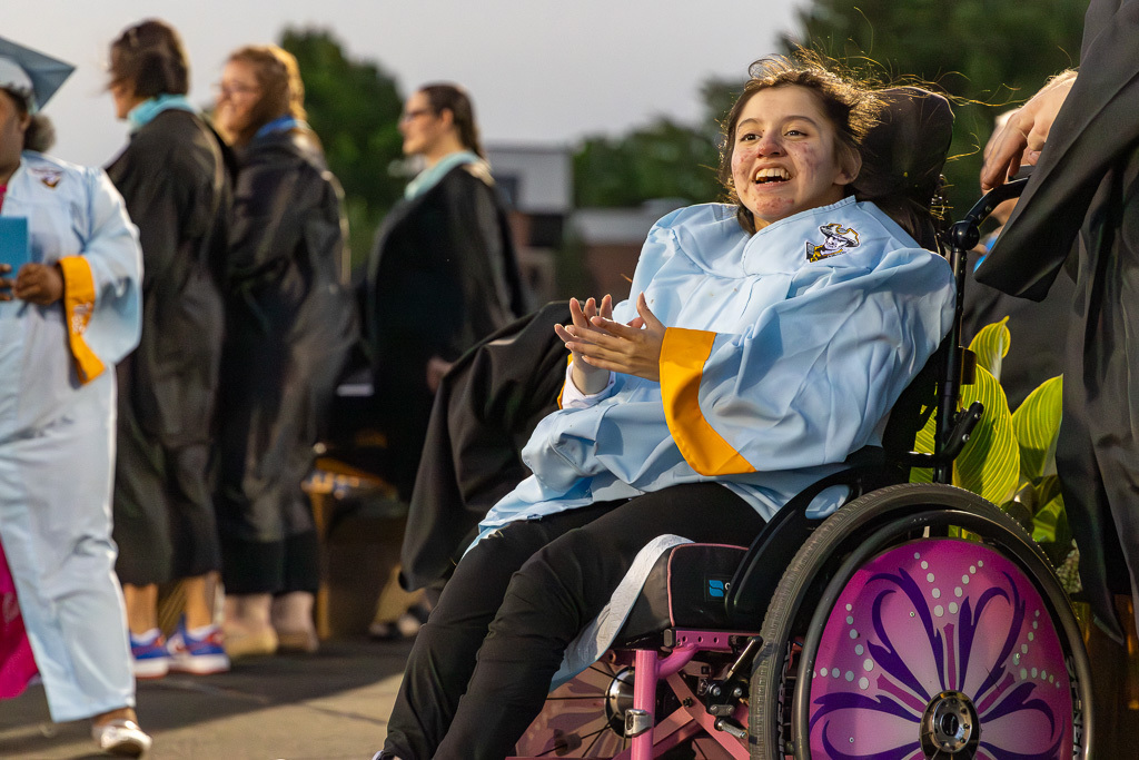 A Putnam City West graduate smiles and claps while seated on stage in a wheelchair during graduation.