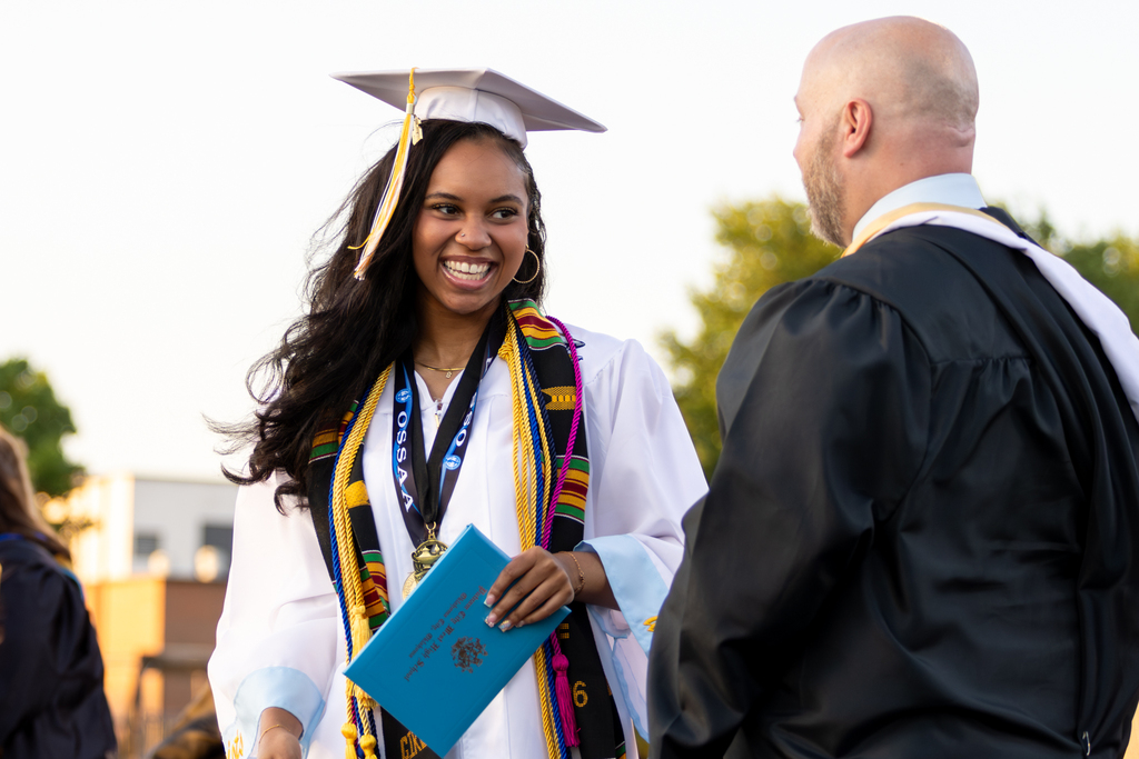 A Putnam City West graduate smiles while receiving a diploma cover from a staff member.