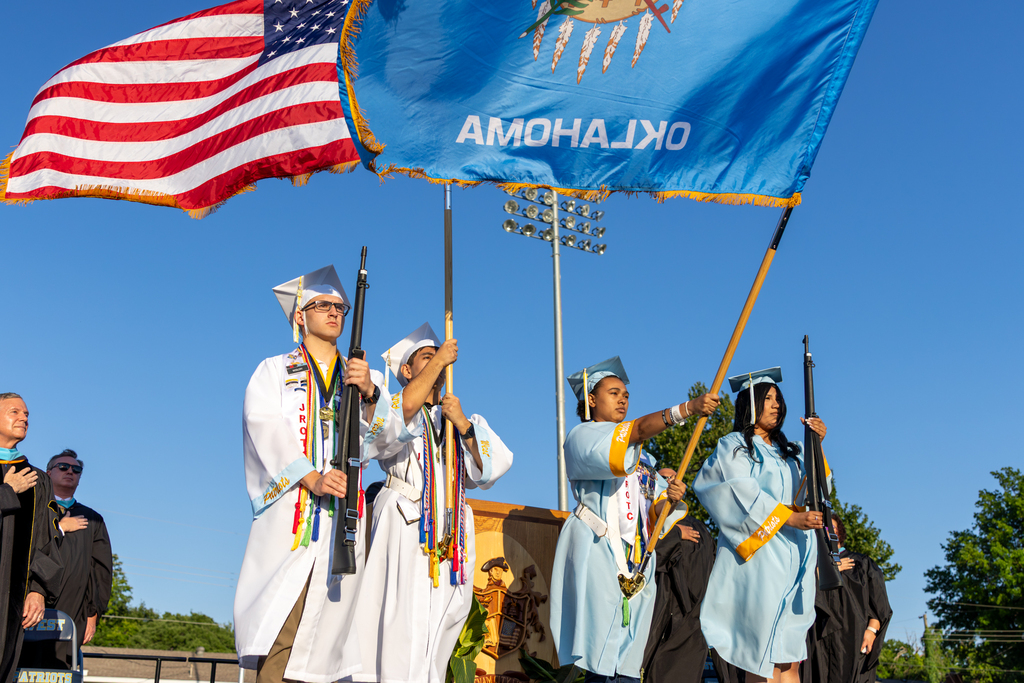 Putnam City West graduates in white and light blue caps and gowns present the flags during the graduation ceremony.