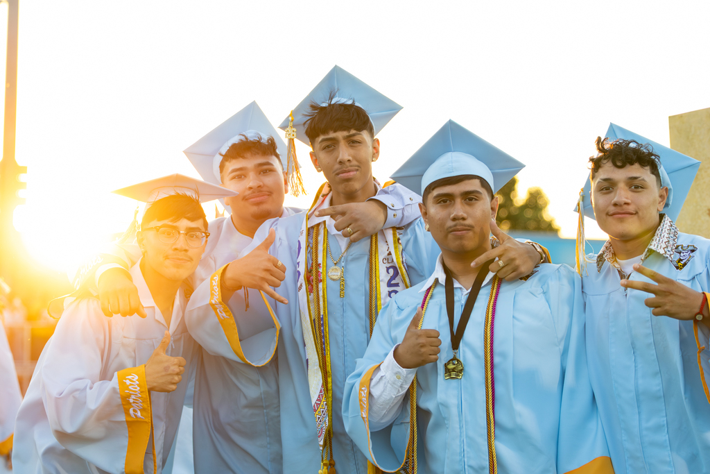 Five Putnam City West graduates in light blue caps and gowns pose together in the evening sun.