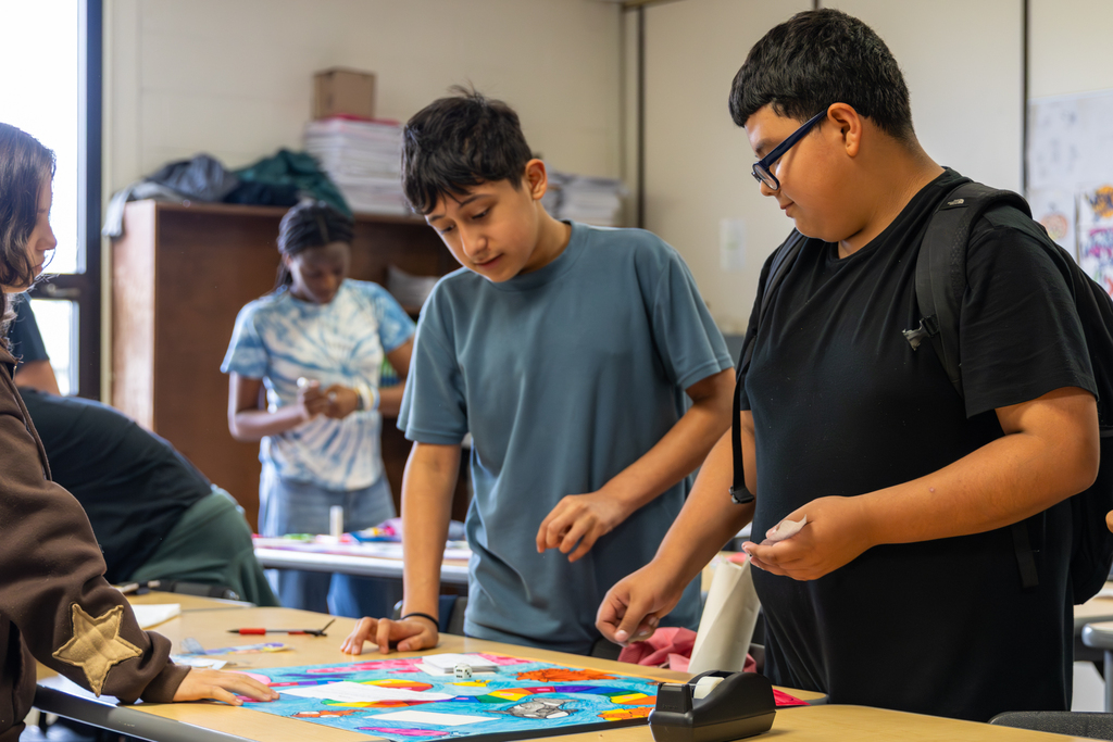 Hefner Middle School students gather around a colorful student-made math board game on a classroom table.