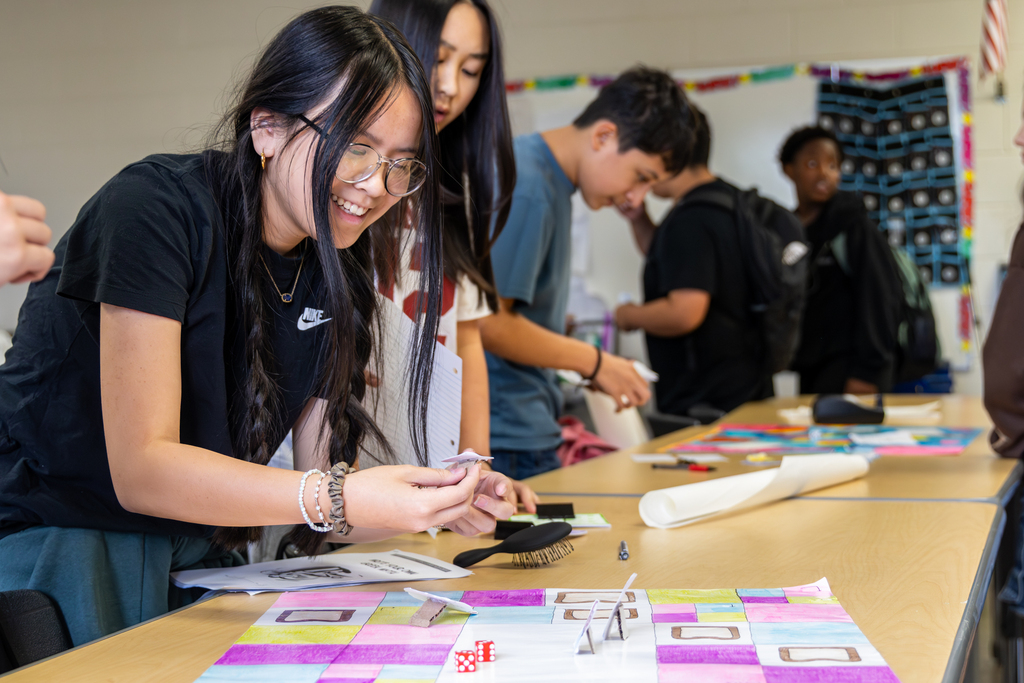 Hefner Middle School students work together at a table with handmade game pieces, dice and a colorful math board game.