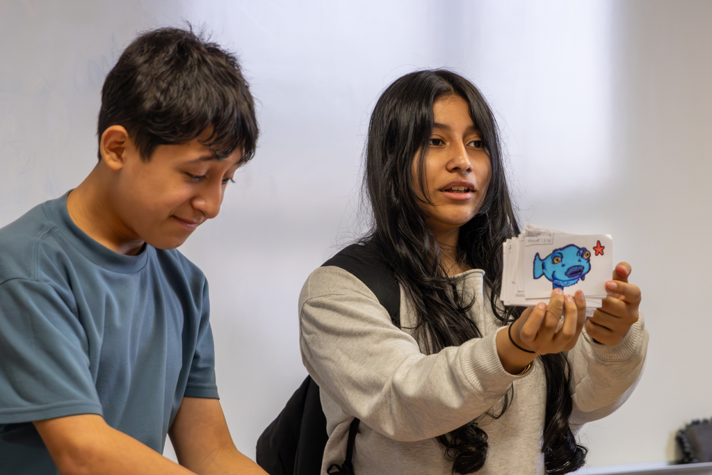 Two Hefner Middle School students share handmade game cards featuring colorful drawings during their math board game project.