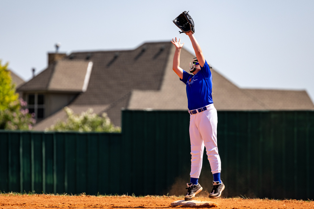 A student jumps beside a base and stretches her glove overhead to make a catch.