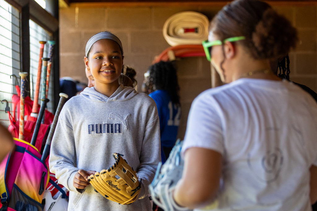 A Hefner Middle School student holds a softball glove while talking with a teammate in the dugout during tryouts.