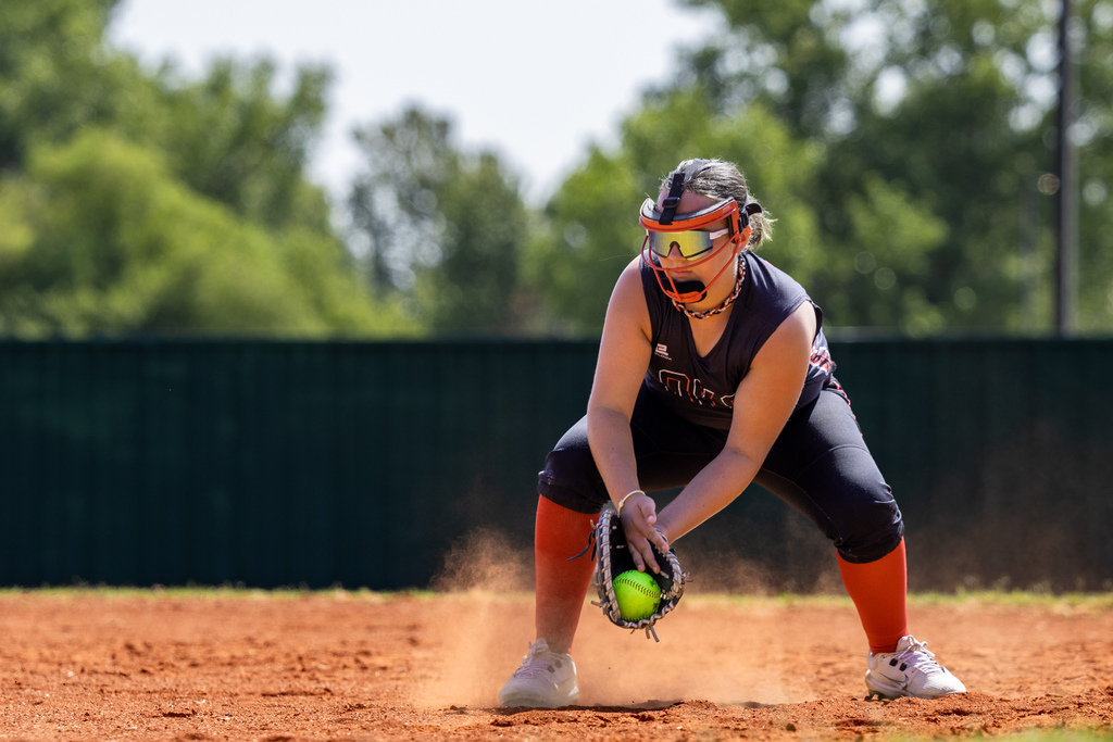 A student fields a ground ball as dust rises from the infield.
