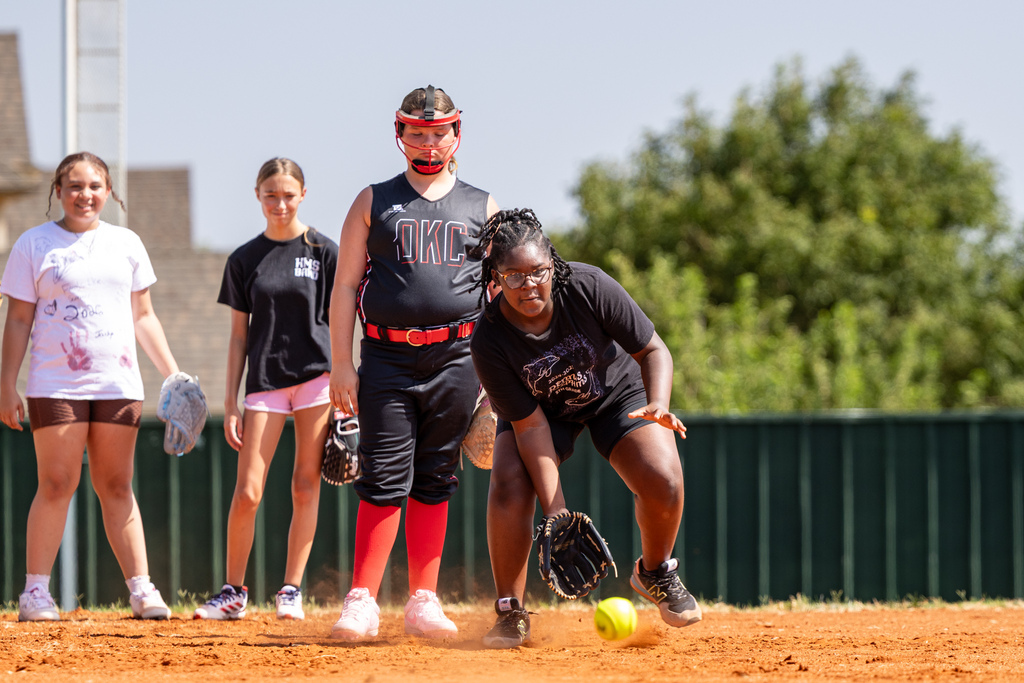 A student reaches for a ground ball while three other players wait behind her.