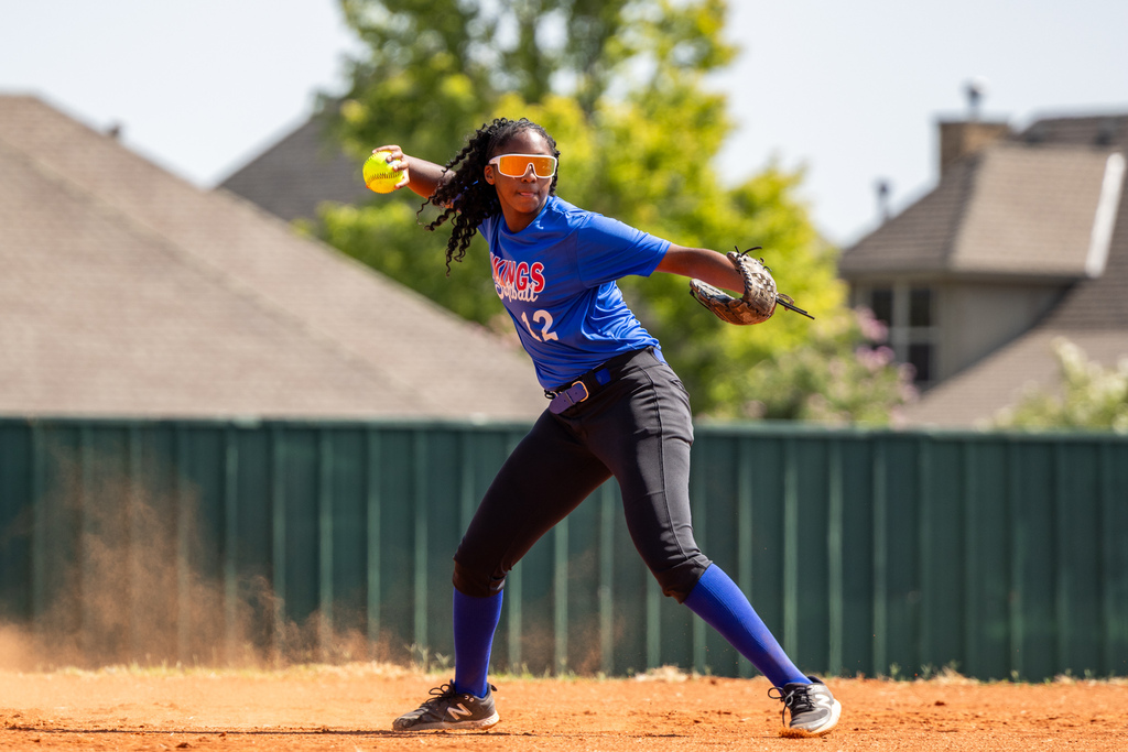 A student winds up to throw a softball across the infield.