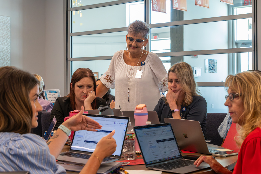 Administrators review information together on laptops during a small-group session.