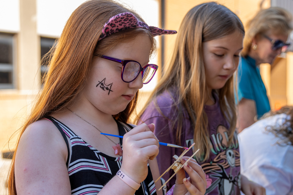 A student paints a small wooden craft while another student works beside her during a back-to-school event at Western Oaks Middle School
