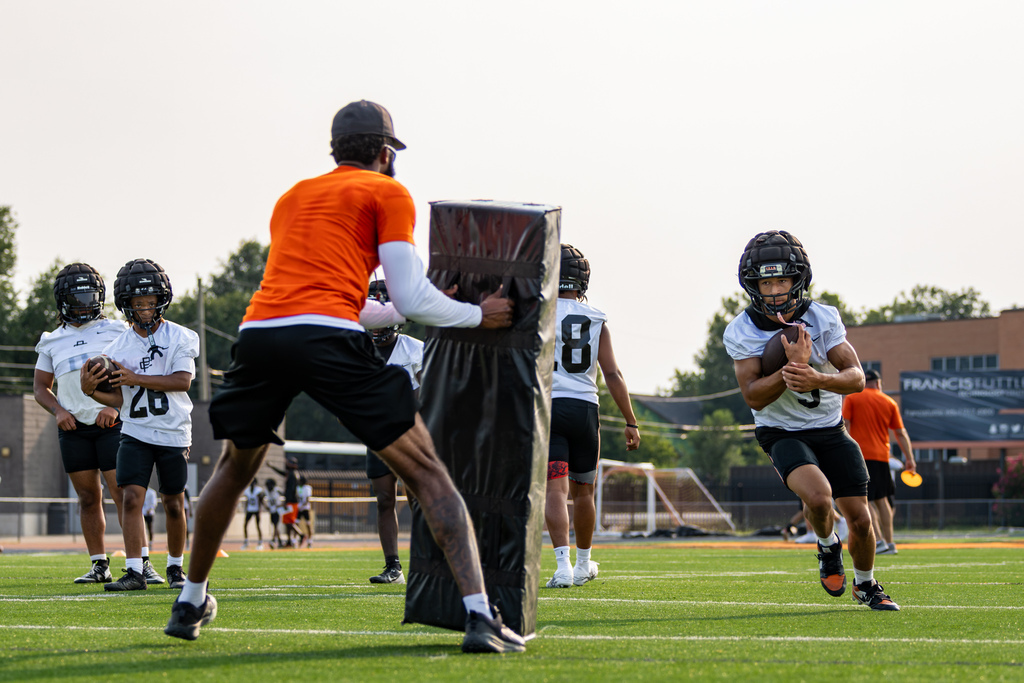 A Putnam City High football player carries the ball toward a blocking pad during a contact drill.