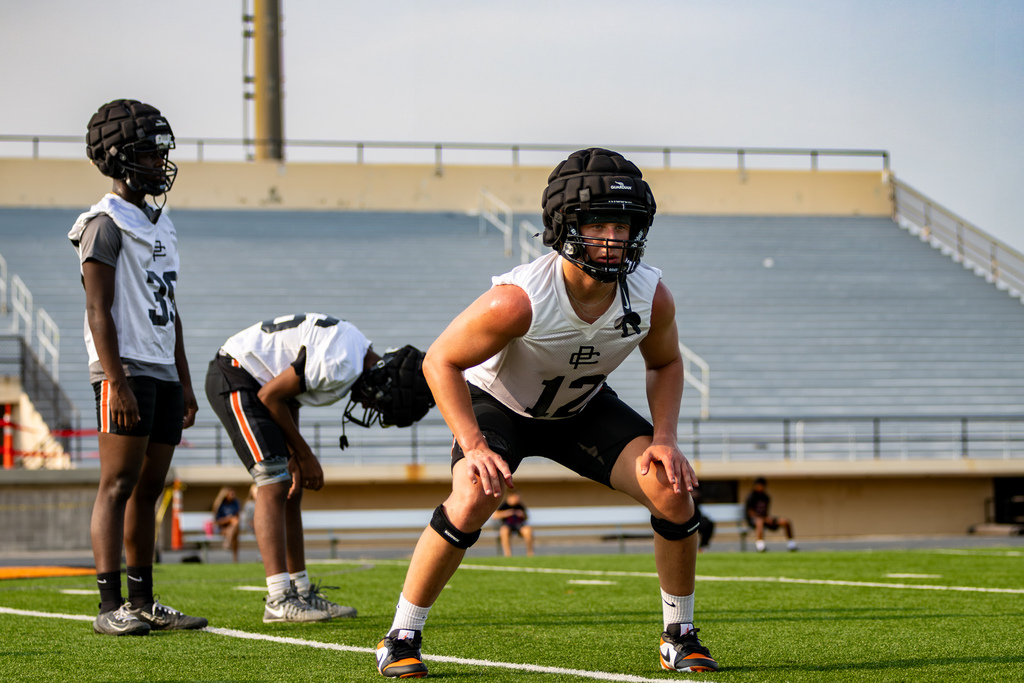 A Putnam City High football player crouches in a ready position during a practice drill as teammates stand behind him.