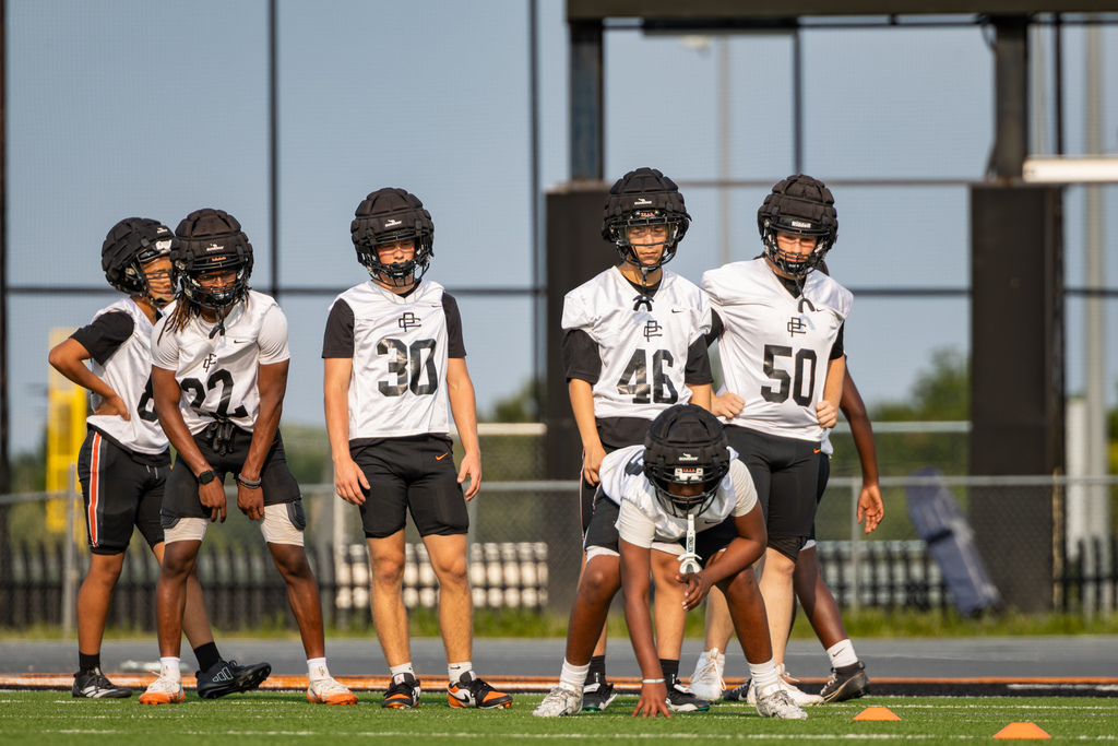 Putnam City High football players line up for a drill, with one player crouched in a three-point stance at the front.