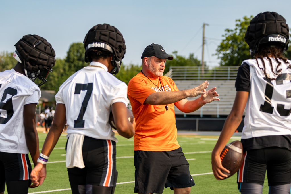 A Putnam City High football coach demonstrates hand positioning while players gather around him during camp.