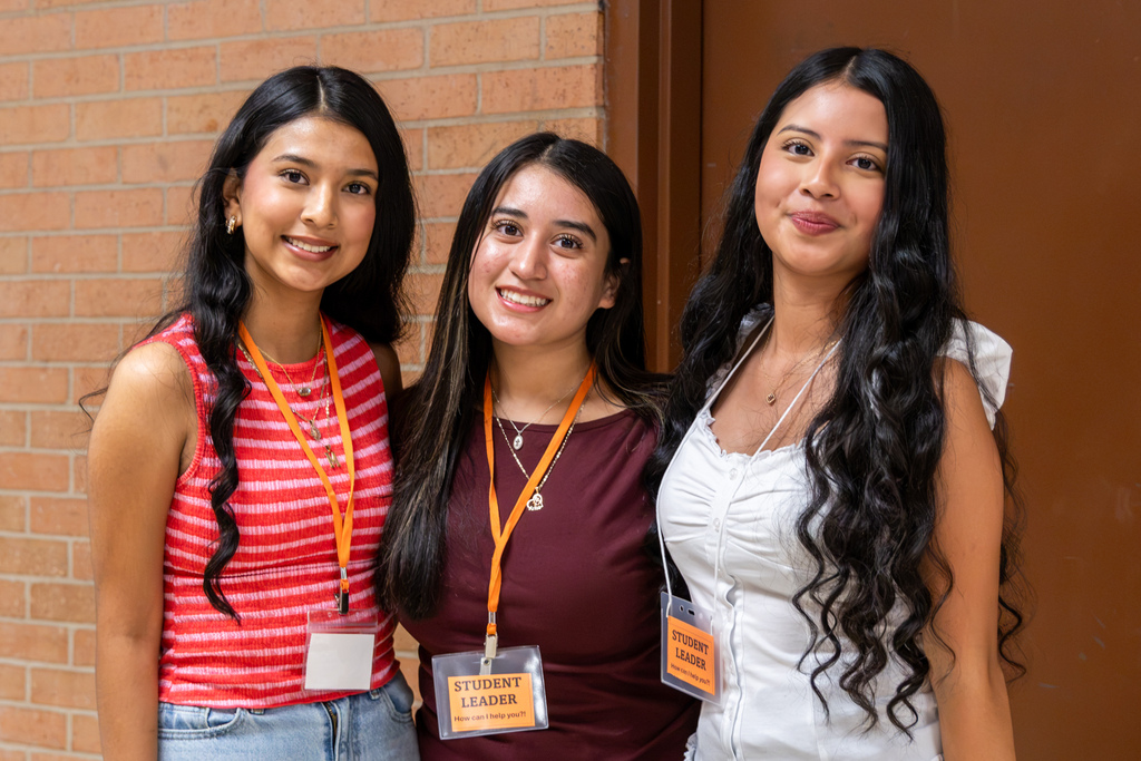 Three high school student leaders smile together inside the school while wearing student leader badges.