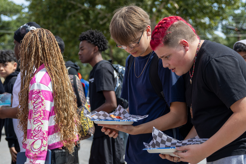 Two Putnam City West students look down at plates of food while classmates gather nearby during the school’s lunchtime Back to School Bash.