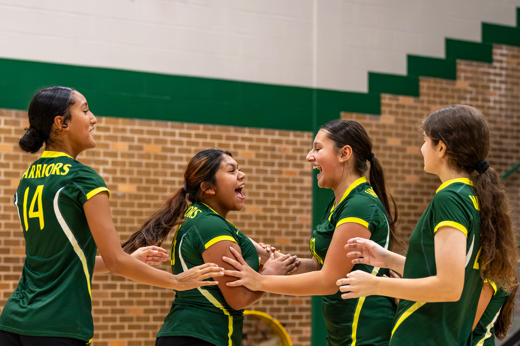 Western Oaks Middle School volleyball players celebrate together on the court, smiling and reaching toward one another after a play.