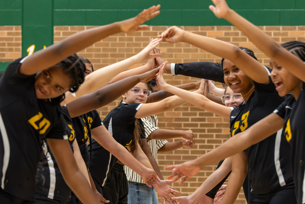 Cooper Middle School volleyball players form a tunnel with their arms as teammates move through, smiling and cheering before the match.