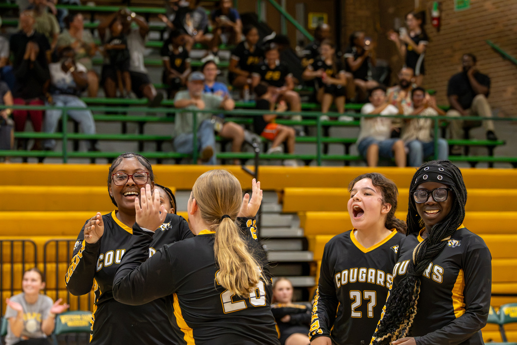 Cooper Middle School volleyball players celebrate together on the court, smiling and raising their hands after a point.