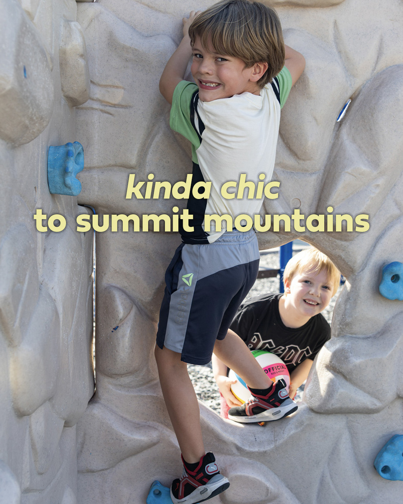 A student climbs a playground rock wall while another student looks up from below. Text reads, “kinda chic to summit mountains.”