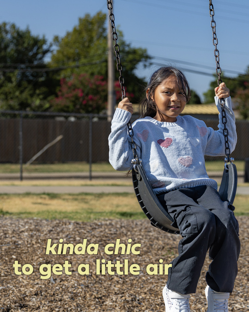 A student swings high against a bright blue sky during recess at Arbor Grove Elementary. Text reads, “kinda chic to get a little air.”