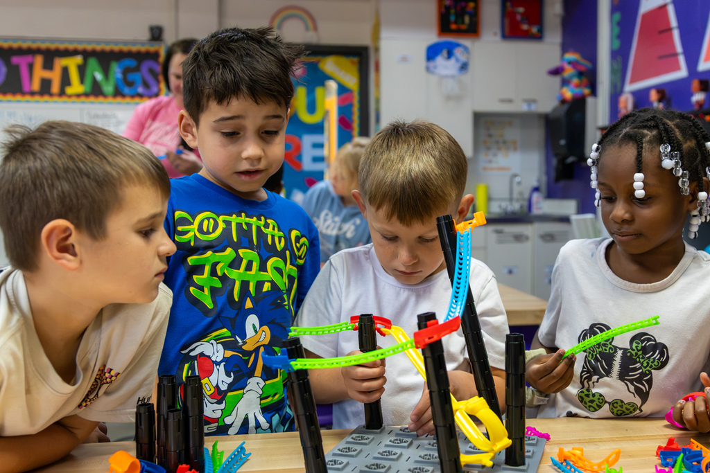 Four Rollingwood Elementary students study a partially built roller coaster as they add and adjust track pieces together.