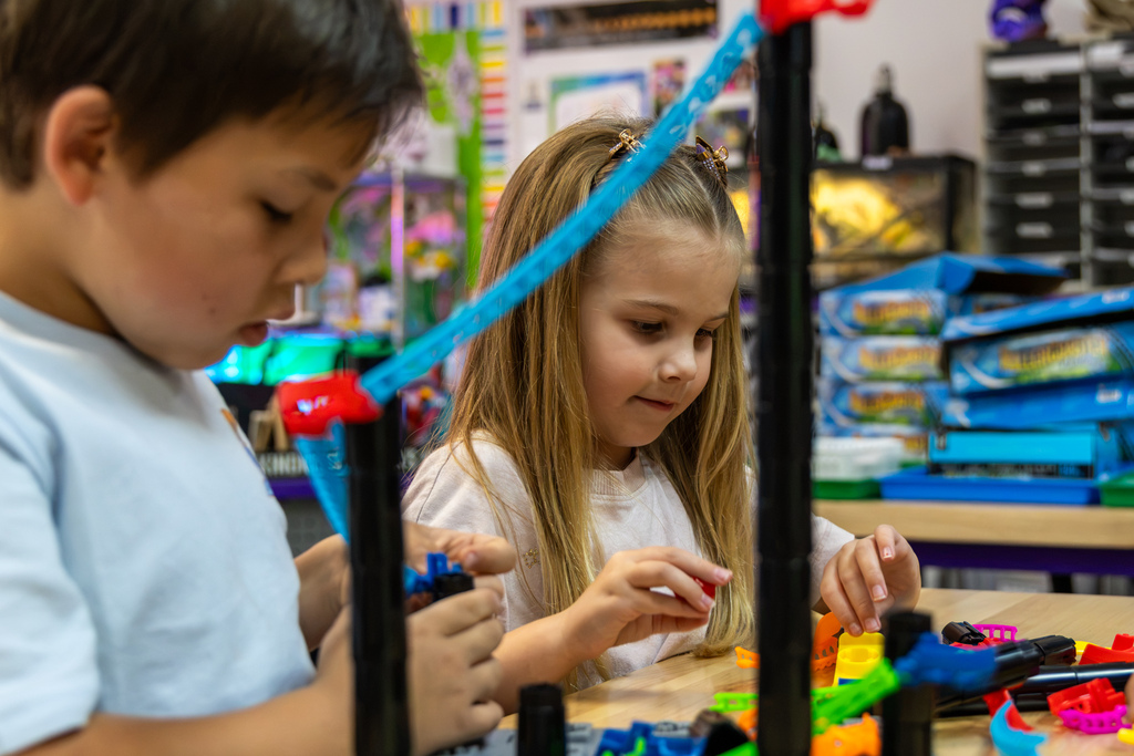 Two Rollingwood Elementary students work together at a table, assembling colorful roller coaster track pieces around tall black supports.