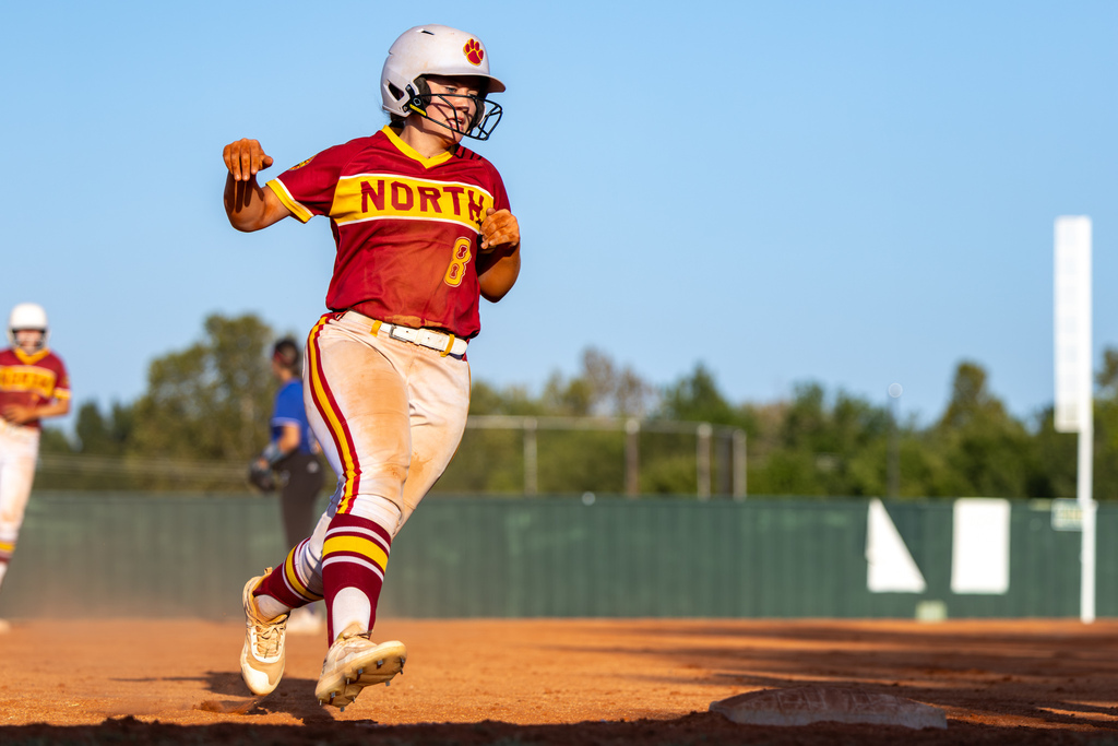 A PC North softball player runs toward a base on the dirt infield, looking toward the play as she rounds the bag.