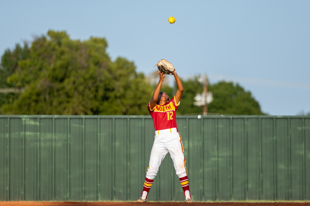 A PC North outfielder stands beneath a high fly ball with both arms raised and her glove open for the catch.