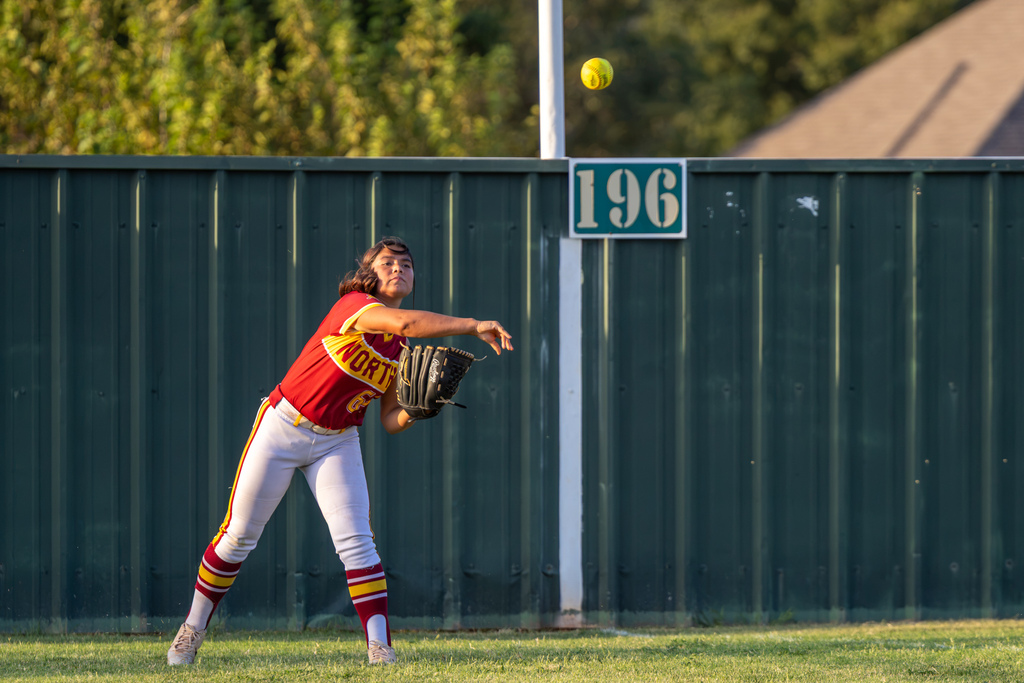 A PC North outfielder throws the softball back toward the infield from near the outfield fence.