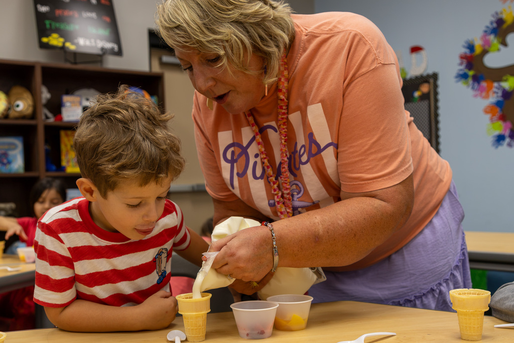 teacher and student fill fruit cup with yogurt