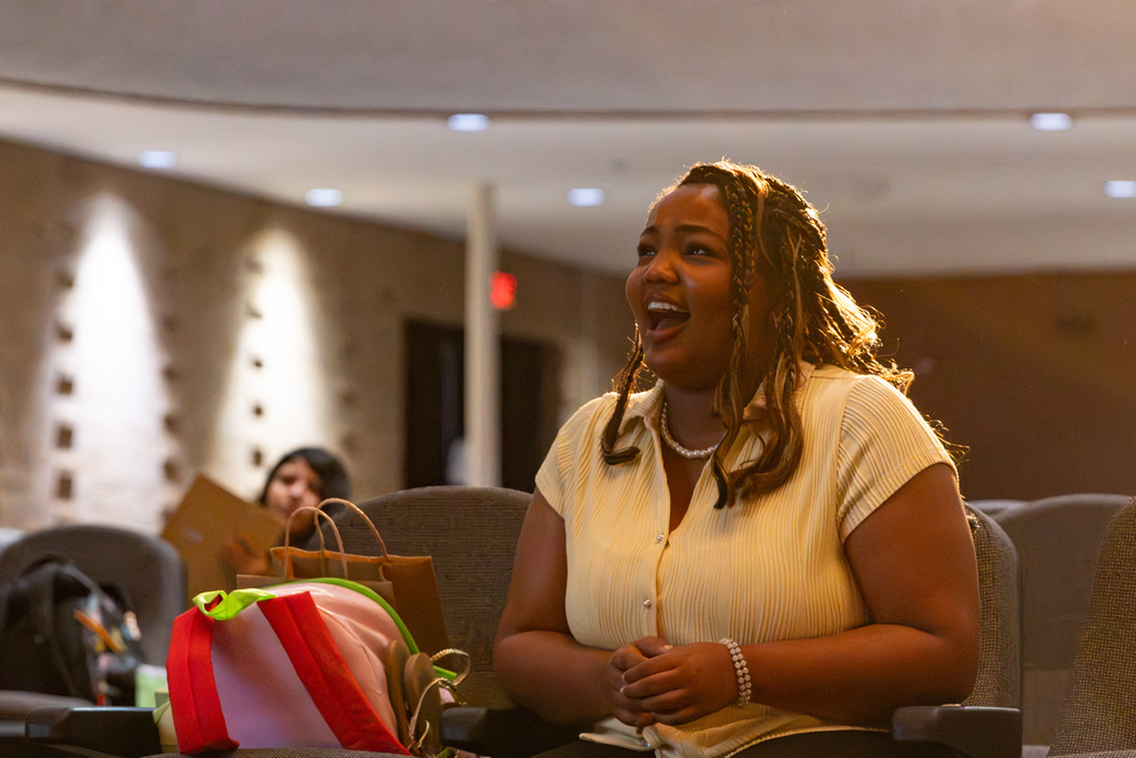A PC High dance student smiles while seated in the auditorium during a class discussion.