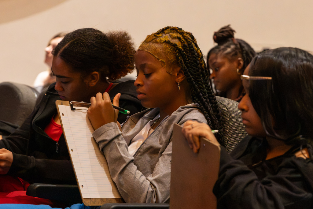Three PC High dance students sit together in auditorium seats, writing on clipboards during a class activity.