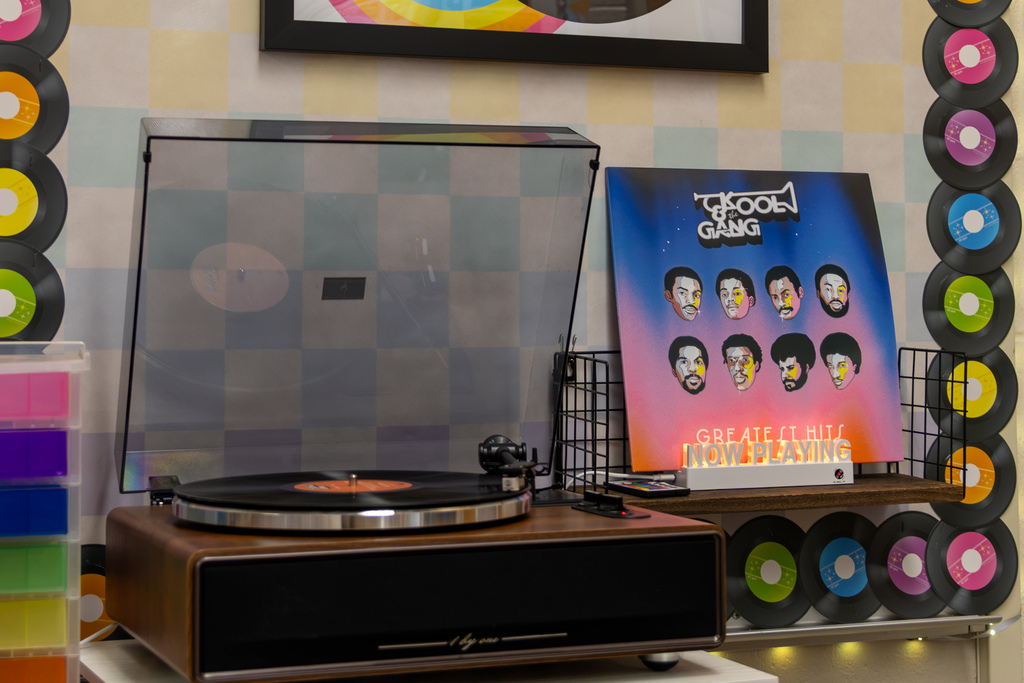 A vinyl record spins on a turntable beside a Kool & the Gang greatest-hits album cover, surrounded by colorful record-themed classroom decor.