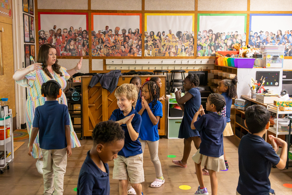 Ms. Wonderly leads first-grade students through a movement game as they walk and gesture around colored spots on the music room floor.
