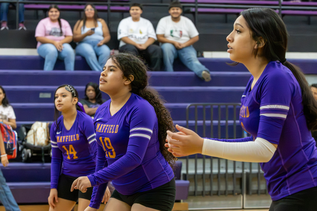 Three Mayfield volleyball players stand ready on the court, watching the play develop in front of them.
