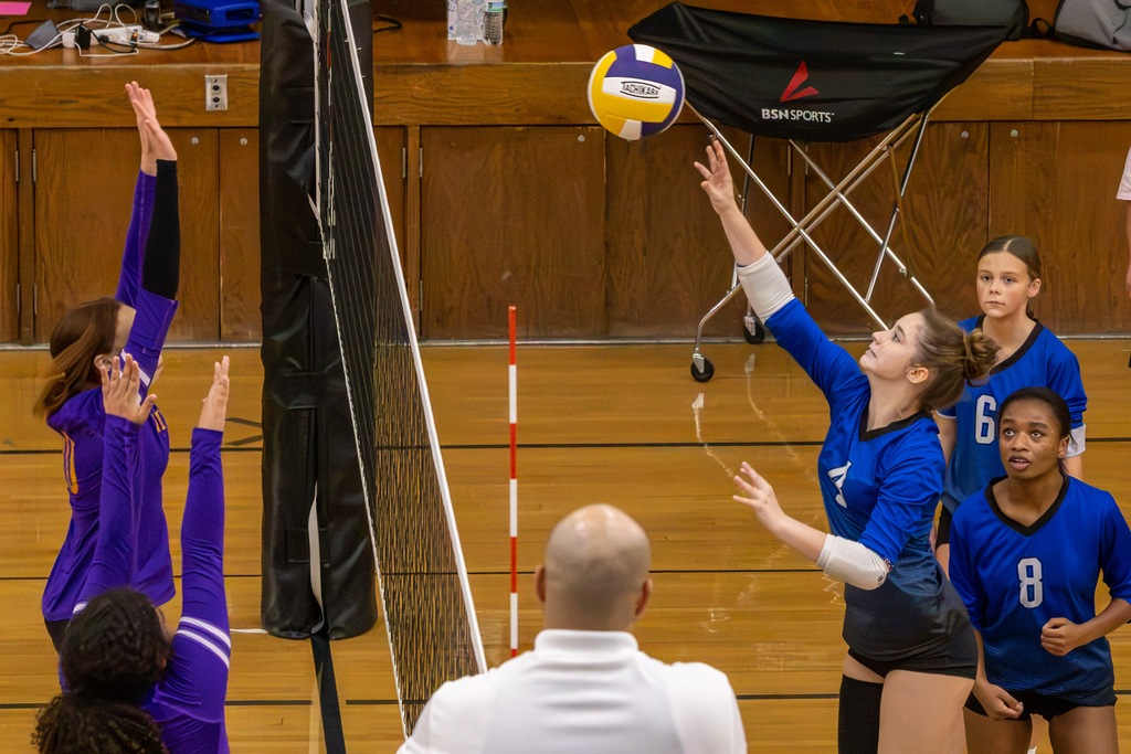 A Hefner player reaches toward the ball at the net as two Mayfield players raise their hands to block.