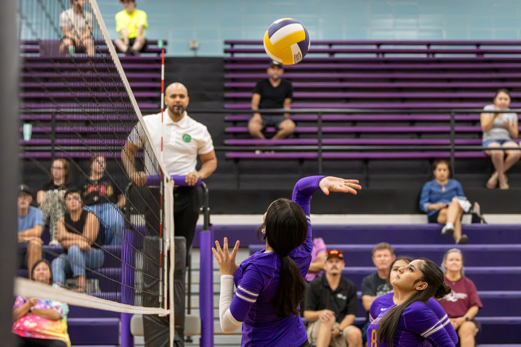 A Mayfield Middle School volleyball player reaches up to hit the ball near the net while a teammate watches from beside her.