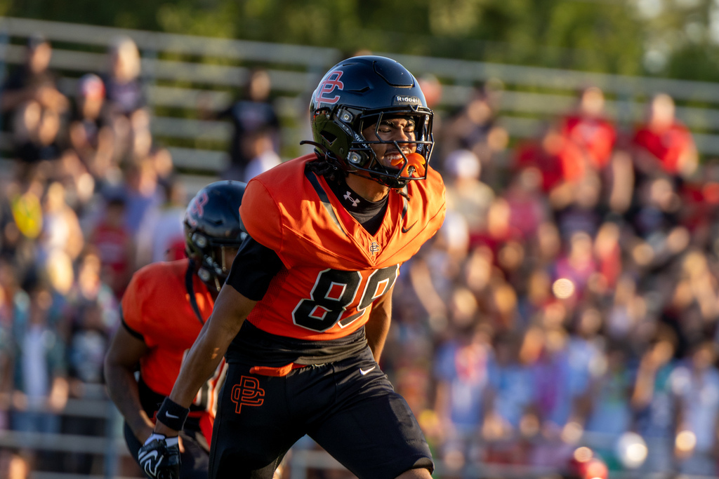 A Putnam City High football player shouts on the field with the packed home stands blurred behind him.