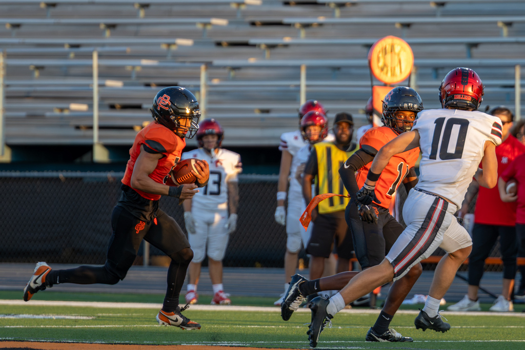 A Putnam City High football player carries the ball behind a blocker as a Yukon defender closes in during the season opener.