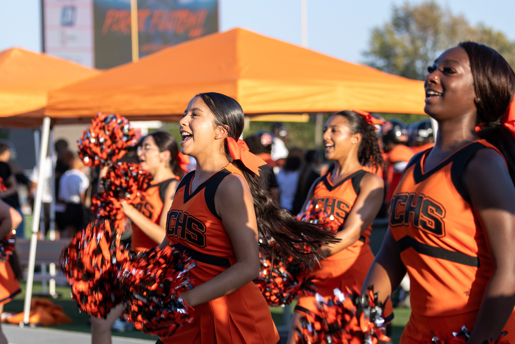 Putnam City High pom members cheer from the sideline in orange and black uniforms before the football game.