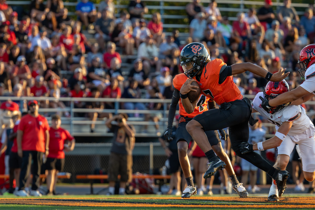Putnam City High No. 7 runs through the Yukon defense as players reach and dive toward him.