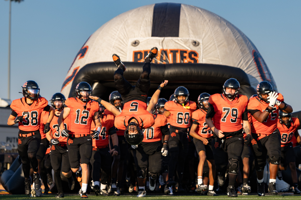 Putnam City High football players run onto the field beneath the inflatable Pirates entrance as one player flips upside down at the front of the team.