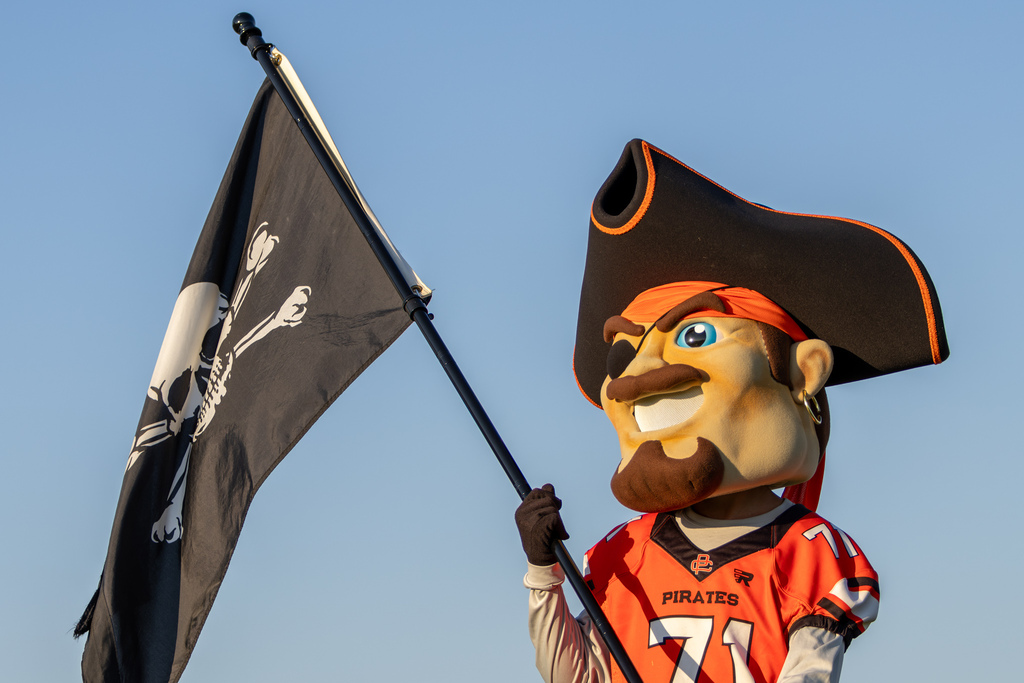 The Putnam City High Pirate mascot holds a black pirate flag against the clear evening sky.