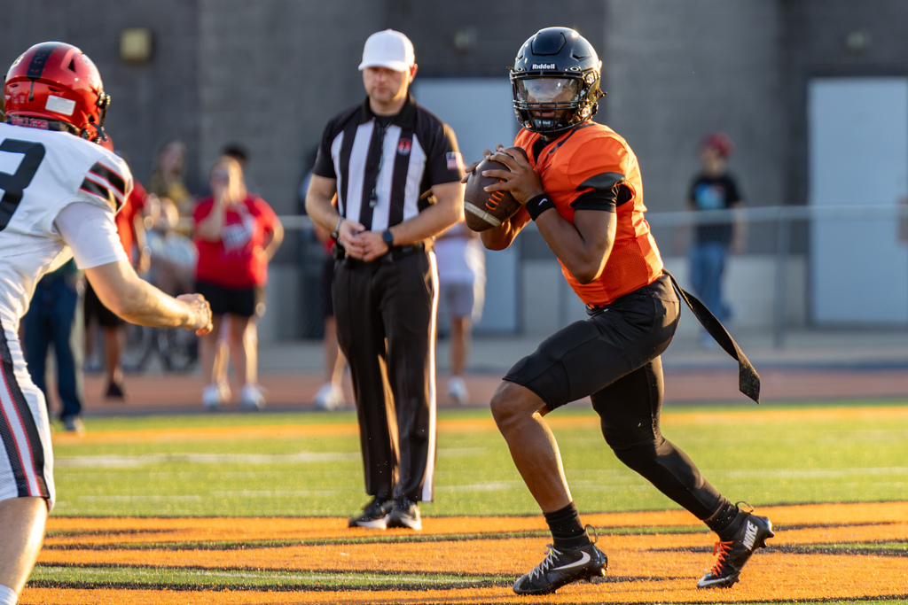 A Putnam City High quarterback holds the football and looks downfield as a Yukon defender approaches during the season opener.
