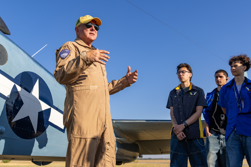 Aviation students listen to a pilot explain a historic military aircraft.