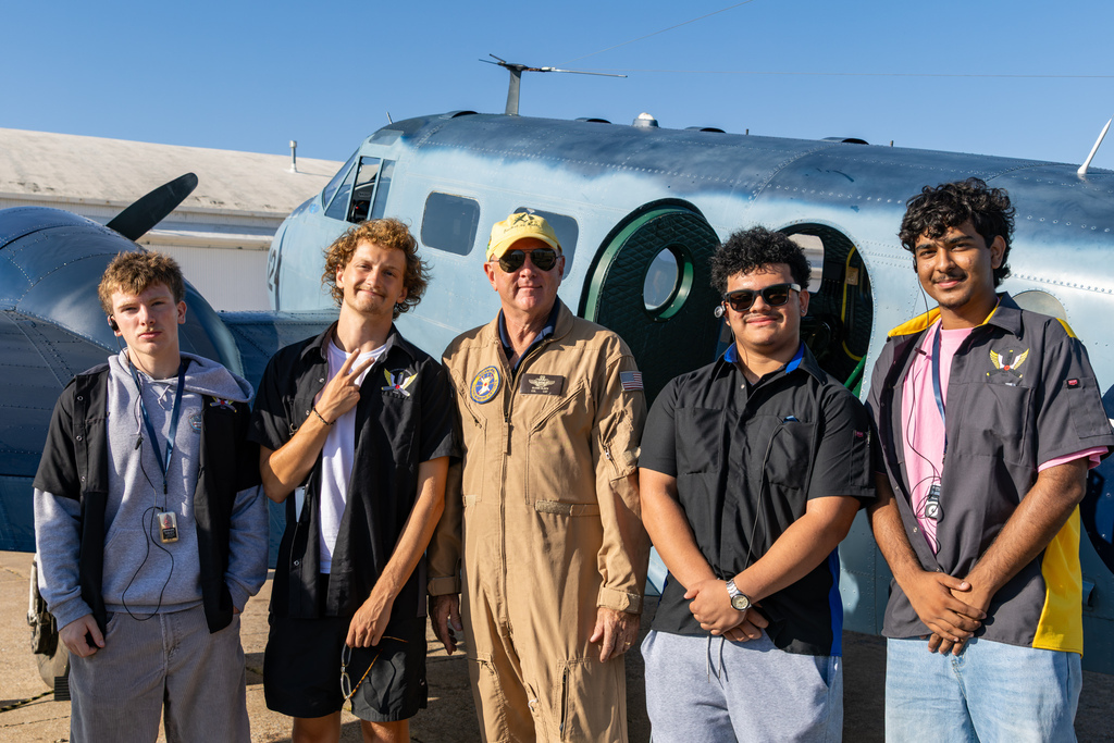 Four aviation students pose with a pilot in front of a historic aircraft.