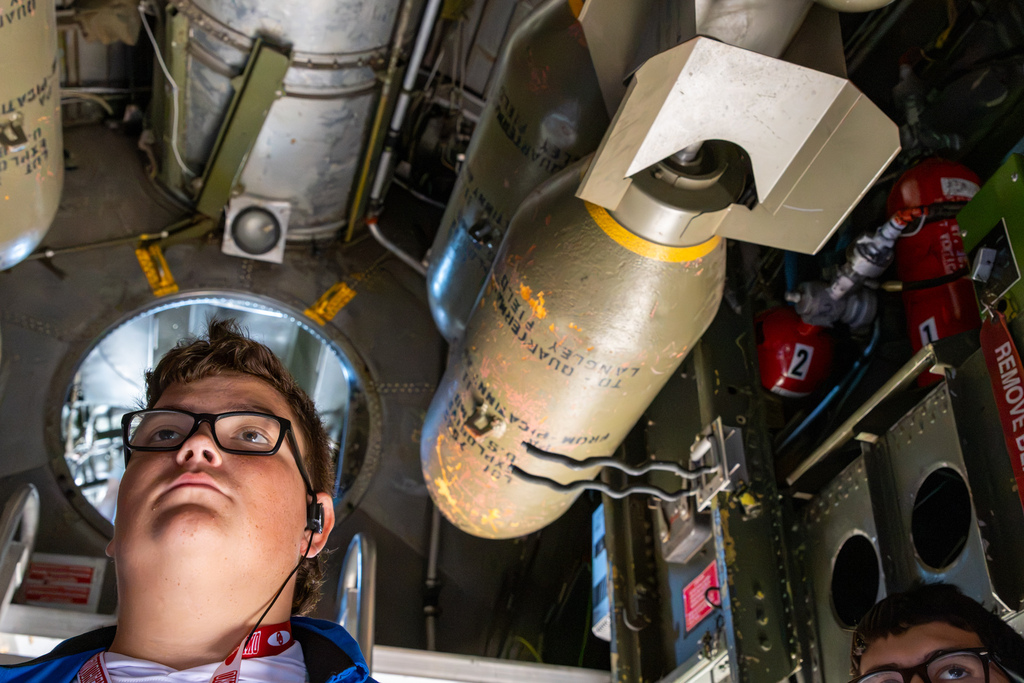 An aviation student looks up at equipment mounted inside a historic aircraft.